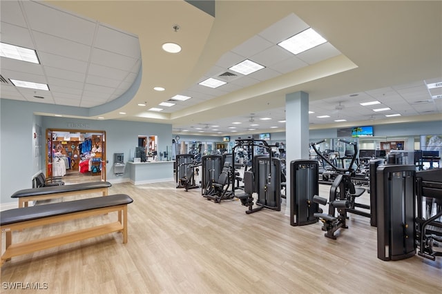 gym with light wood-type flooring, a tray ceiling, and a drop ceiling