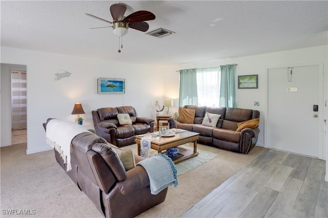 living room with ceiling fan, a textured ceiling, and light wood-type flooring