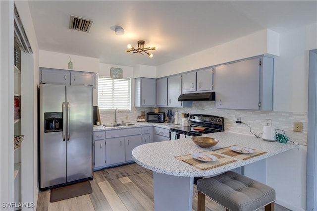 kitchen with kitchen peninsula, appliances with stainless steel finishes, a kitchen breakfast bar, light wood-type flooring, and sink