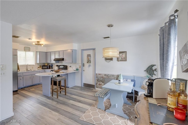 kitchen featuring kitchen peninsula, gray cabinetry, decorative light fixtures, a kitchen breakfast bar, and stainless steel refrigerator