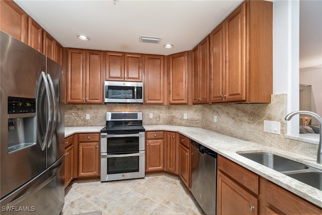 kitchen with stainless steel appliances, backsplash, light tile patterned floors, light stone countertops, and sink