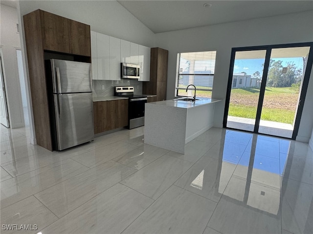 kitchen with stainless steel appliances, a center island with sink, sink, vaulted ceiling, and tasteful backsplash