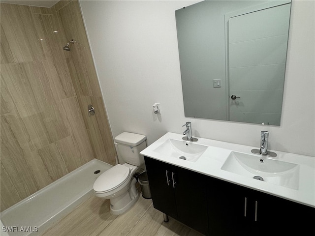 bathroom with toilet, hardwood / wood-style floors, vanity, and a tile shower