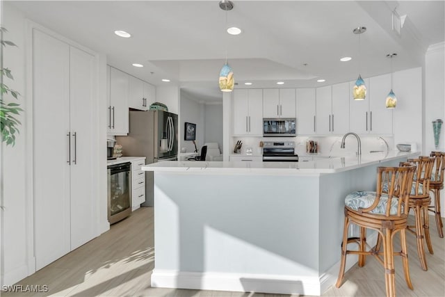 kitchen with white cabinetry, kitchen peninsula, pendant lighting, appliances with stainless steel finishes, and light wood-type flooring