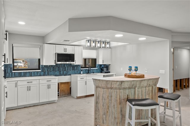 kitchen with a breakfast bar area, sink, white cabinetry, and backsplash