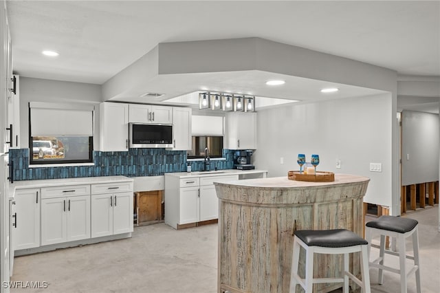 435 Donora Blvd, Fort Myers Beach, FL 33931 - kitchen with white cabinets, a sink, stainless steel microwave, decorative backsplash, and a kitchen island