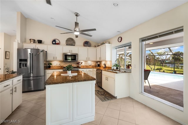 kitchen with appliances with stainless steel finishes, white cabinets, vaulted ceiling, and a kitchen island