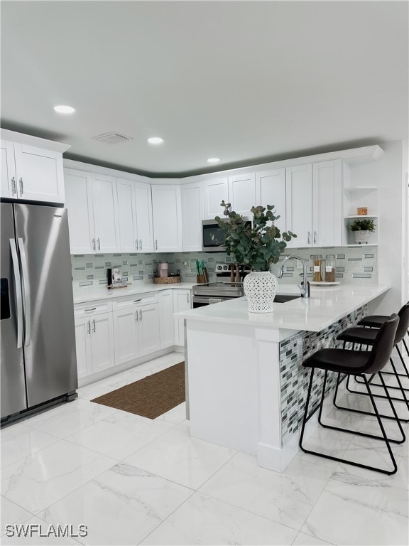 kitchen featuring kitchen peninsula, white cabinetry, stainless steel appliances, decorative backsplash, and a breakfast bar area