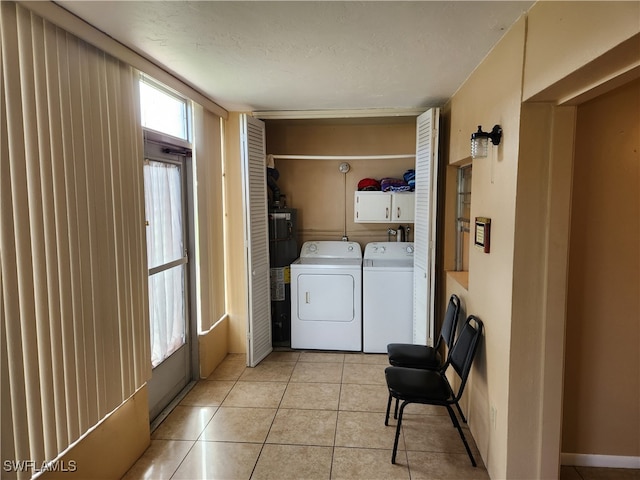 laundry room featuring cabinets, light tile patterned floors, a textured ceiling, and washing machine and clothes dryer