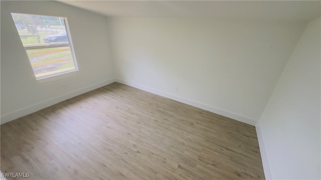 spare room with lofted ceiling and light wood-type flooring