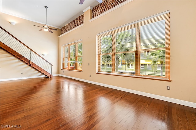 unfurnished living room with ceiling fan, crown molding, wood-type flooring, and a high ceiling