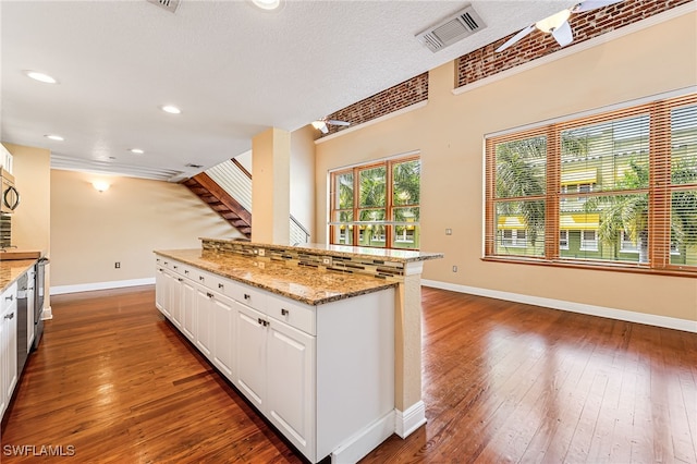 kitchen featuring a textured ceiling, stainless steel appliances, white cabinets, light stone counters, and dark hardwood / wood-style floors