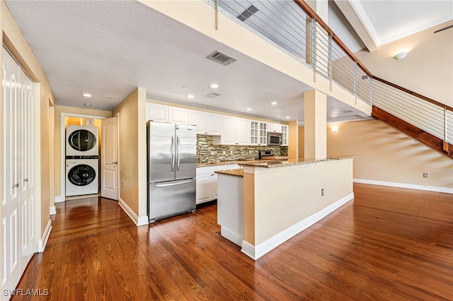 kitchen with white cabinets, appliances with stainless steel finishes, light stone countertops, stacked washer / drying machine, and dark wood-type flooring