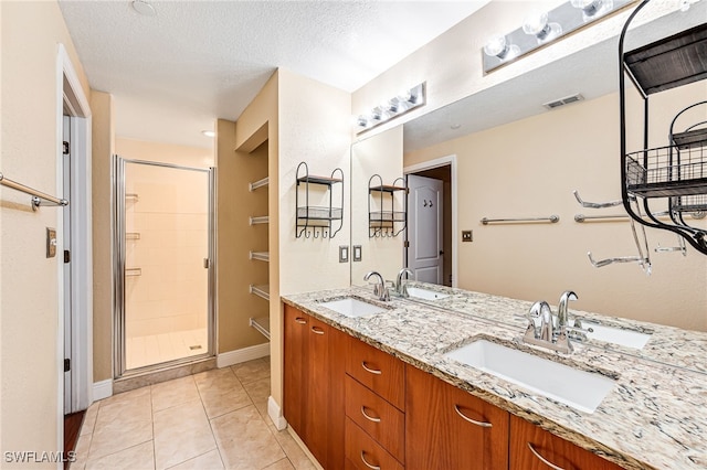 bathroom with a shower with door, a textured ceiling, vanity, and tile patterned flooring