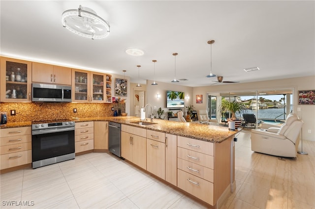 kitchen featuring stainless steel appliances, a peninsula, a sink, open floor plan, and light brown cabinetry