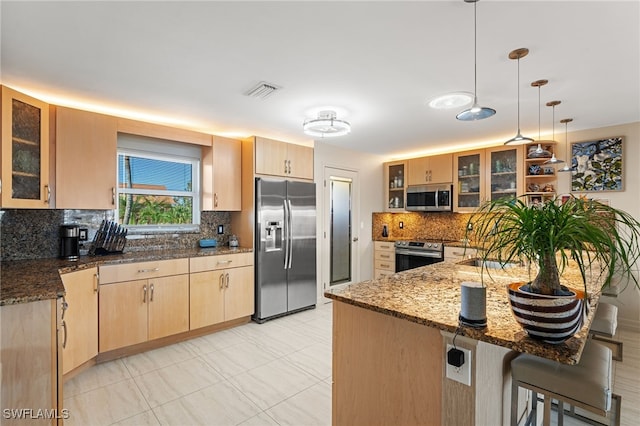 kitchen featuring light brown cabinets, hanging light fixtures, stainless steel appliances, dark stone counters, and a breakfast bar area