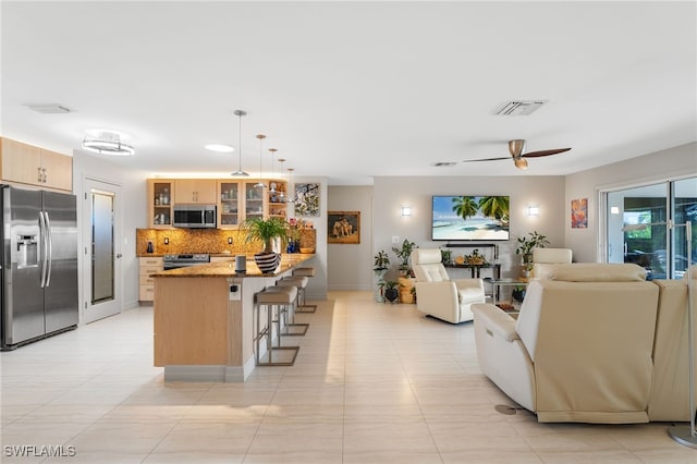 kitchen with a breakfast bar, hanging light fixtures, ceiling fan, decorative backsplash, and appliances with stainless steel finishes