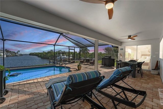 pool at dusk with ceiling fan, a patio, a water view, and a lanai