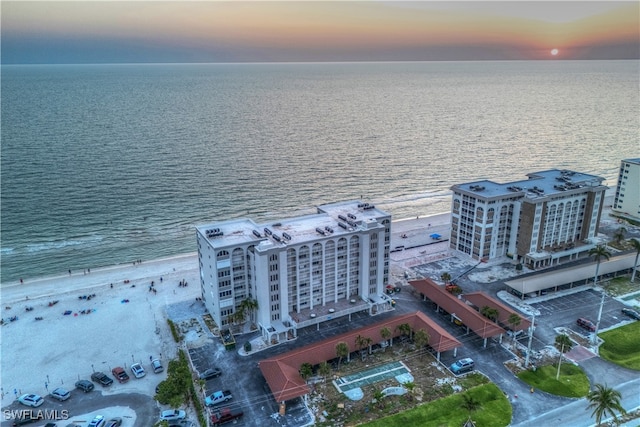 aerial view at dusk with a water view and a view of the beach