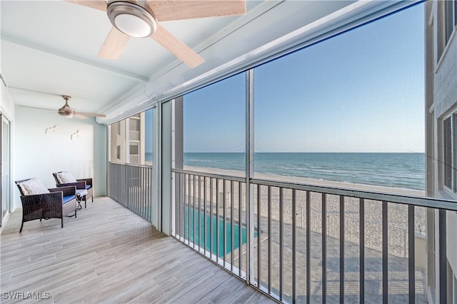 sunroom with a view of the beach, beam ceiling, a water view, and ceiling fan