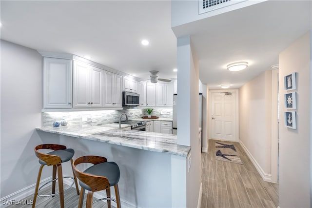 kitchen featuring kitchen peninsula, decorative backsplash, a kitchen bar, white cabinetry, and stainless steel appliances