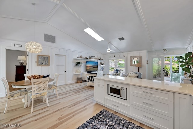 kitchen featuring white cabinetry, white microwave, decorative light fixtures, and light wood-type flooring