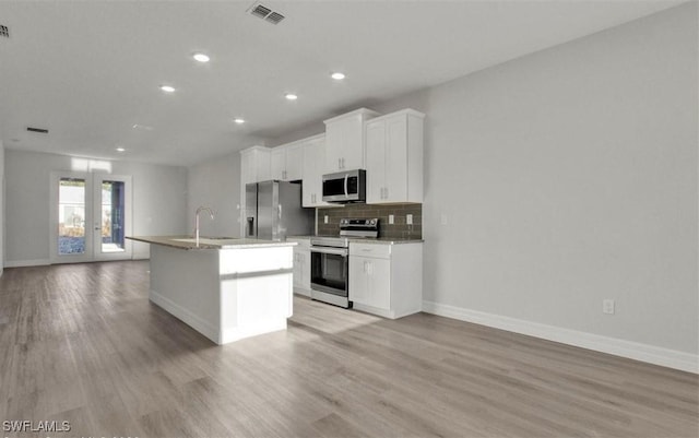 kitchen featuring french doors, light wood-type flooring, stainless steel appliances, a center island with sink, and white cabinets