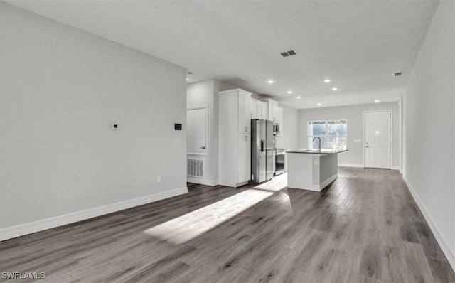 interior space with appliances with stainless steel finishes, a center island with sink, white cabinetry, and dark hardwood / wood-style floors