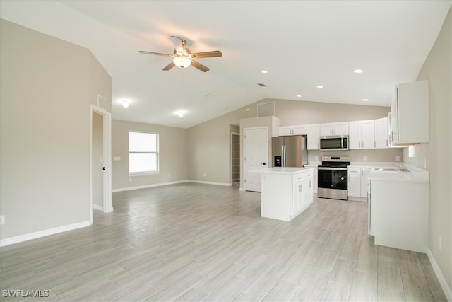 kitchen with ceiling fan, appliances with stainless steel finishes, vaulted ceiling, light hardwood / wood-style flooring, and a center island