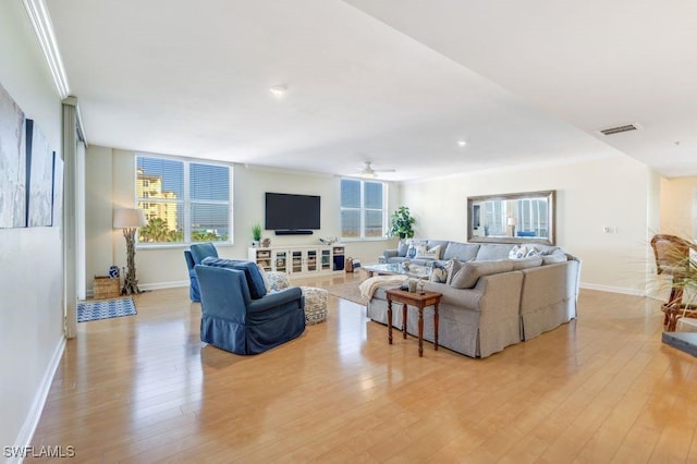 living room featuring light wood-type flooring, baseboards, visible vents, and crown molding