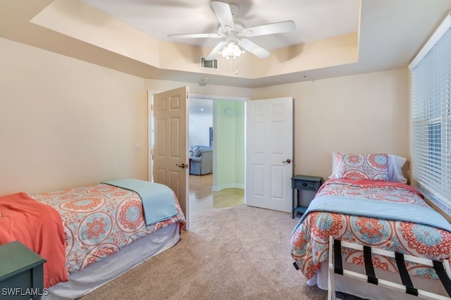 carpeted bedroom with a raised ceiling and ceiling fan