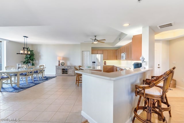 kitchen with white appliances, light brown cabinetry, kitchen peninsula, decorative light fixtures, and light tile patterned floors