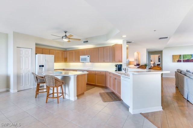 kitchen with a breakfast bar area, kitchen peninsula, light wood-type flooring, light brown cabinetry, and white appliances