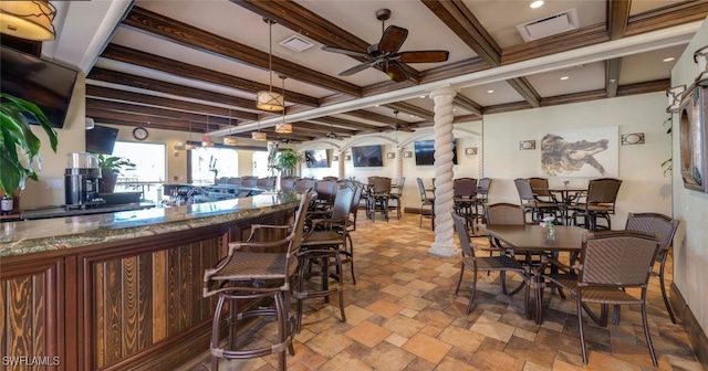 dining space featuring indoor bar, decorative columns, beamed ceiling, and ceiling fan