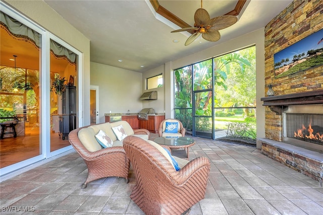 sunroom featuring an outdoor stone fireplace and ceiling fan