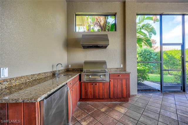 kitchen with light stone countertops, wall chimney range hood, sink, stainless steel fridge, and tile patterned floors