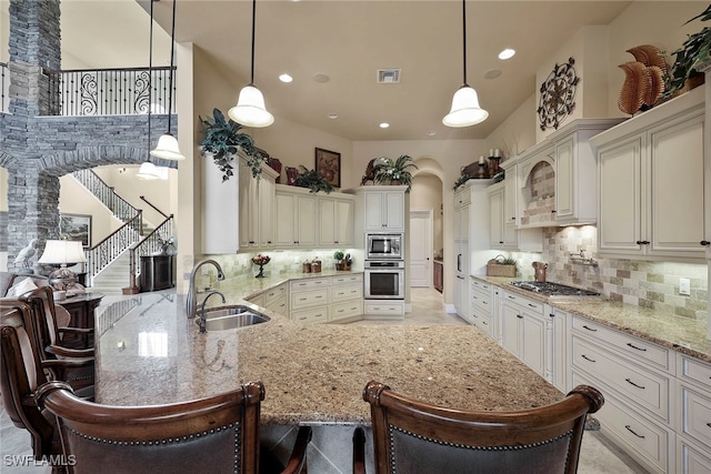 kitchen featuring decorative backsplash, appliances with stainless steel finishes, a breakfast bar, sink, and decorative light fixtures