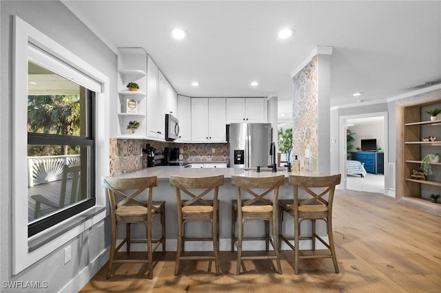 kitchen featuring white cabinetry, stainless steel appliances, light hardwood / wood-style flooring, kitchen peninsula, and a breakfast bar