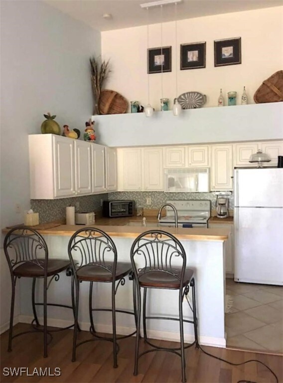 kitchen featuring white appliances, tasteful backsplash, a kitchen bar, kitchen peninsula, and dark hardwood / wood-style floors