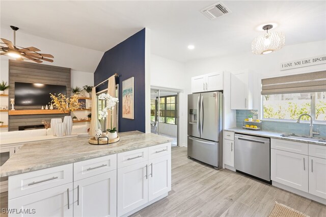 kitchen with white cabinets, hanging light fixtures, appliances with stainless steel finishes, light hardwood / wood-style flooring, and sink