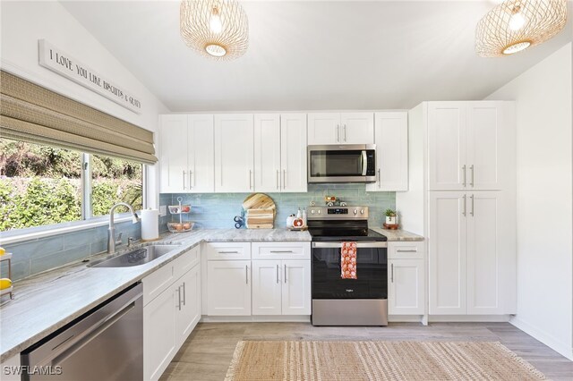 kitchen featuring stainless steel appliances, sink, vaulted ceiling, white cabinets, and light hardwood / wood-style floors