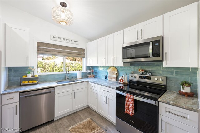 kitchen with lofted ceiling, appliances with stainless steel finishes, white cabinetry, light hardwood / wood-style flooring, and sink