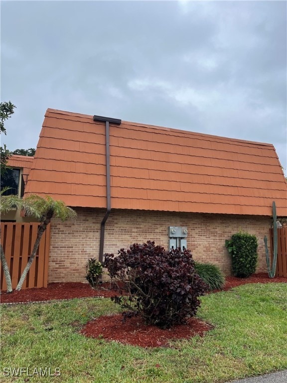 view of side of property with mansard roof, brick siding, a lawn, and fence