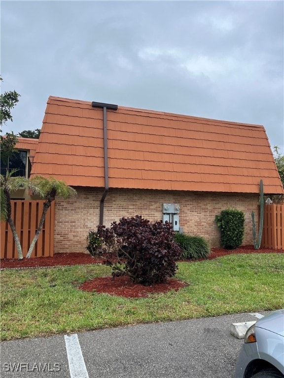 view of side of property featuring mansard roof, brick siding, a lawn, and fence