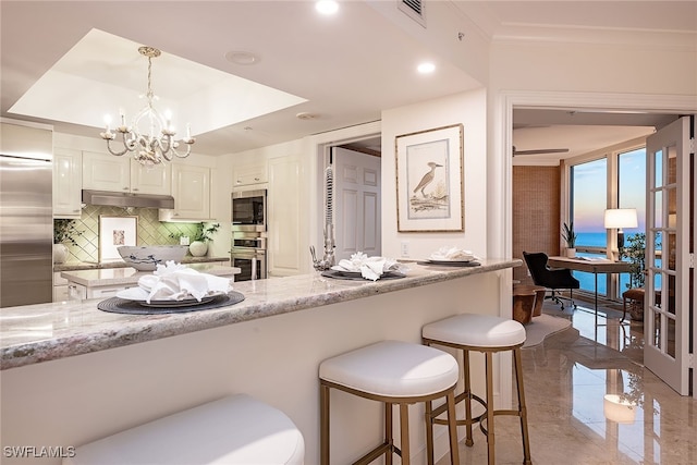 kitchen with pendant lighting, appliances with stainless steel finishes, tasteful backsplash, light stone counters, and white cabinetry