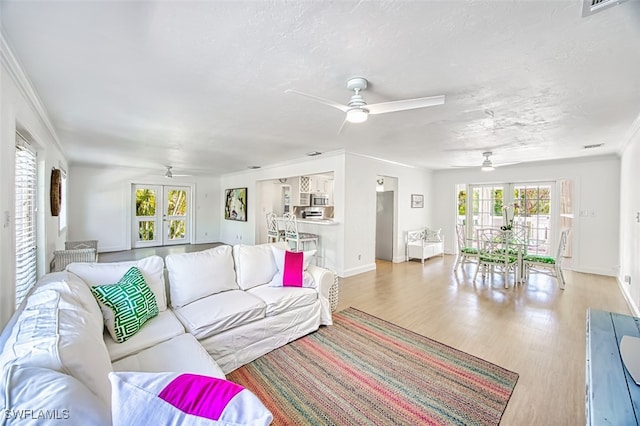 living room with a textured ceiling, ceiling fan, light wood-type flooring, and crown molding