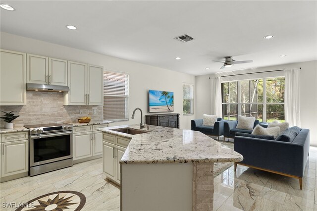 kitchen with stainless steel range with electric stovetop, a center island with sink, sink, ceiling fan, and light stone countertops