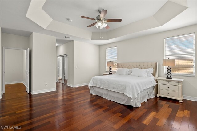 bedroom with ceiling fan, a raised ceiling, dark wood-type flooring, and multiple windows