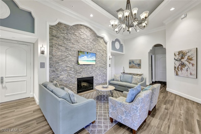 living room with a fireplace, wood-type flooring, an inviting chandelier, and ornamental molding