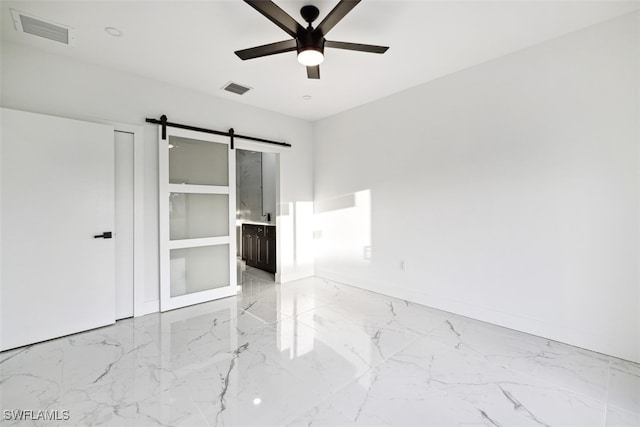 unfurnished bedroom with ensuite bath, a barn door, and ceiling fan